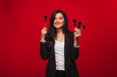 Kırmızı arka planda makyaj fırçaları tutan kız