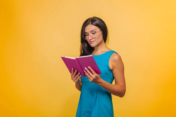 Chica con gafas sobre un fondo amarillo en un vestido azul de lectura —  Fotos de Stock