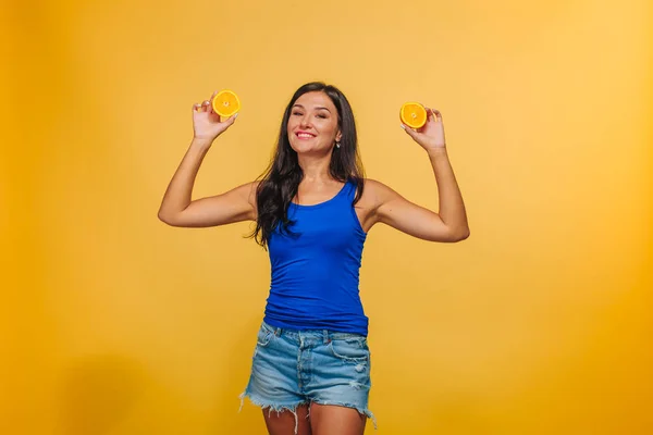 Menina em um fundo amarelo com laranjas . — Fotografia de Stock