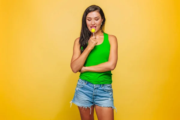 Девушка на желтом фоне ест леденец — стоковое фото