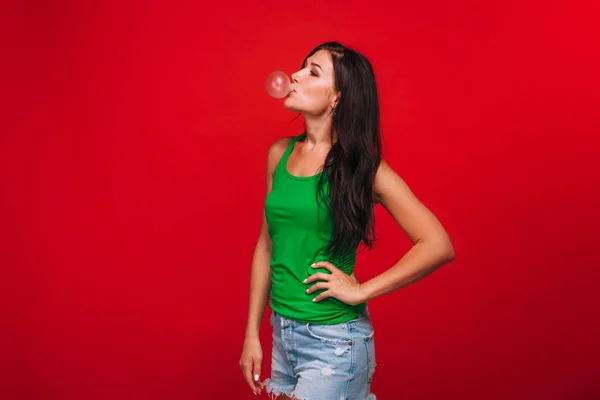 Menina em um fundo vermelho soprando bolhas de chiclete — Fotografia de Stock