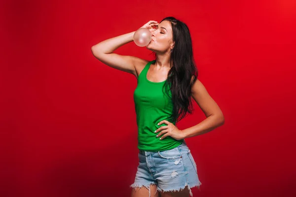 Девушка на красном фоне выдувает пузыри жвачки — стоковое фото