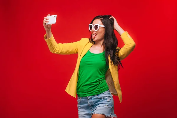 Menina em um fundo vermelho na jaqueta leva uma selfie no telefone — Fotografia de Stock