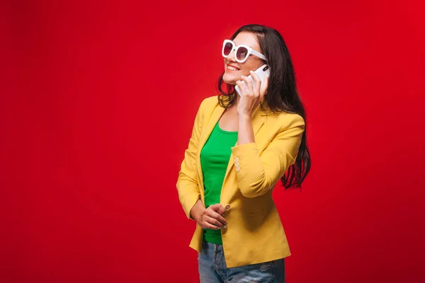 Девушка на красном фоне в желтой куртке разговаривает по телефону — стоковое фото