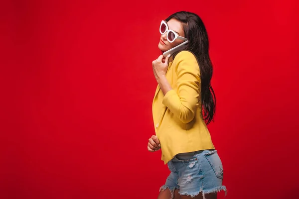 전화통화하는 노란색 재킷을 입은 빨간 배경의 소녀 — 스톡 사진