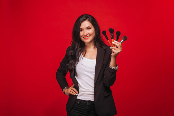 Girl holding makeup brushes on red background