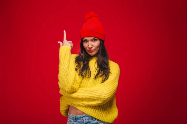 Chica en suéter amarillo y sombrero sobre fondo rojo Muestra los dedos u — Foto de Stock