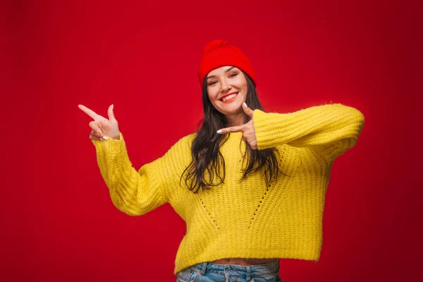 Chica en suéter amarillo y sombrero sobre fondo rojo, muestra a la izquierda — Foto de Stock