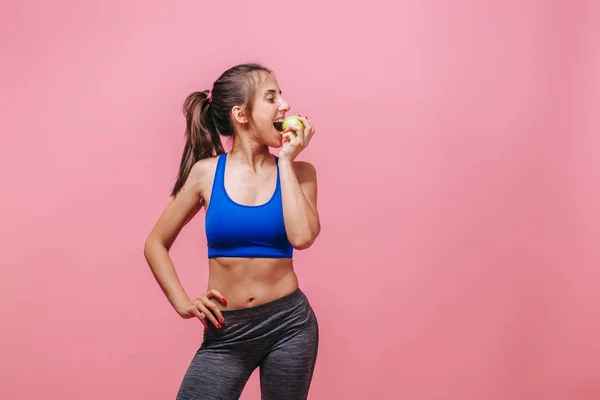 Menina magro mordendo uma maçã verde em um fundo rosa — Fotografia de Stock