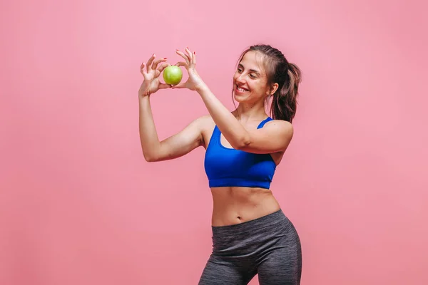 Menina magro segurando maçã verde no fundo rosa — Fotografia de Stock