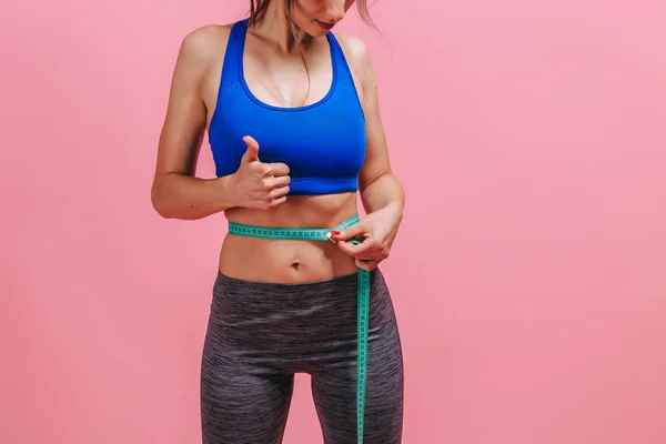 Flaco chica medidas cintura y muestra el pulgar en rosa fondo —  Fotos de Stock