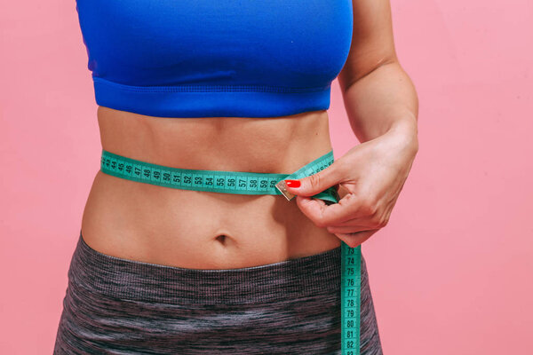 девушка измеряет талию на розовом фоне крупным планом
