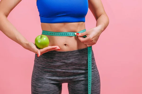 Chica mide la cintura y muestra verde manzana sobre fondo rosa — Foto de Stock