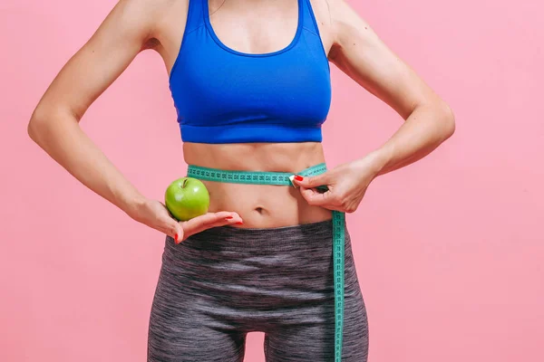 Chica mide la cintura y muestra verde manzana sobre fondo rosa — Foto de Stock