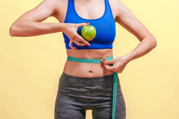 Chica mide la cintura y muestra verde manzana sobre fondo amarillo — Foto de Stock