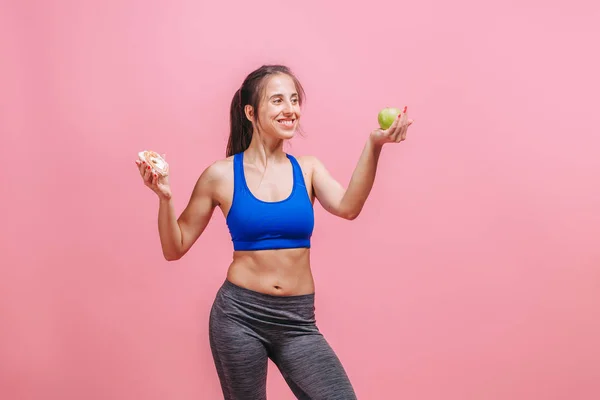 Menina em um fundo rosa segurando um bolo e uma maçã — Fotografia de Stock