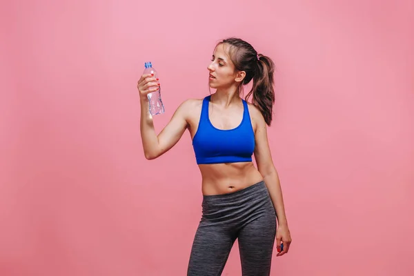 Menina desportiva beber água no fundo rosa — Fotografia de Stock