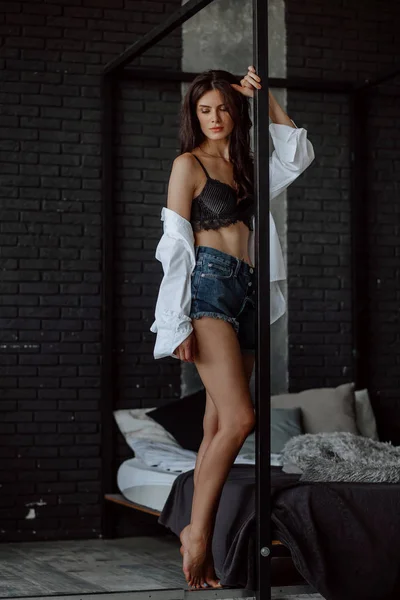 Siyah sütyen seksi esmer kız koyu bir ba yatağın yanında duruyor