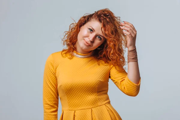 Red curly girl in a yellow dress on a light gray background smil — Stock Photo, Image