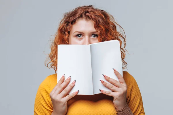 Kızıl saçlı kız yüzünü beyaz bir kitapla örttü.
