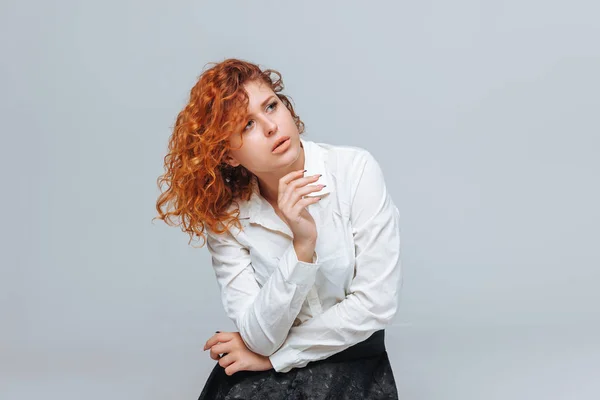 Red headed girl in white shirt thinks on light gray background — Stock Photo, Image