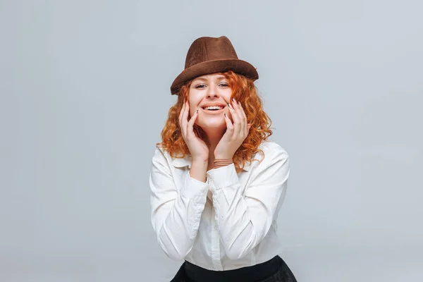 Chica alegre pelirroja en un sombrero marrón sobre un fondo gris en un —  Fotos de Stock