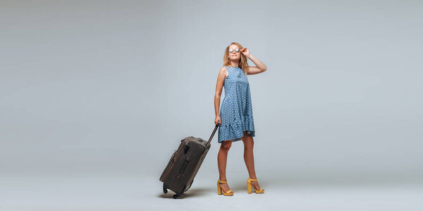 Туристка с чемоданом в солнцезащитных очках на сером фоне
