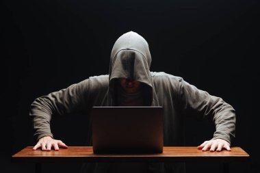 Siyah arka planda dizüstü bilgisayar ile bir kapüşonlu Hacker