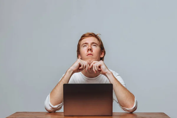 Ein Mann denkt für einen Laptop auf hellem Hintergrund — Stockfoto