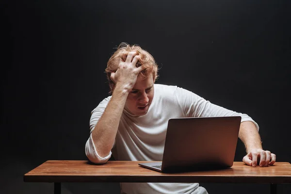 Mann denkt an Laptop in weißem T-Shirt vor schwarzem Hintergrund — Stockfoto