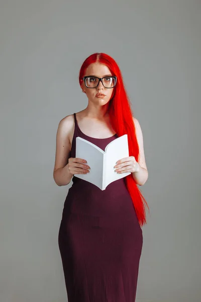 Girl with red long hair wearing glasses with a white book presen — Stock Photo, Image