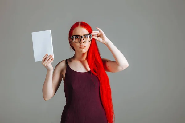 Dziewczyna z czerwonymi długimi włosami noszących okulary z białą książką presen — Zdjęcie stockowe