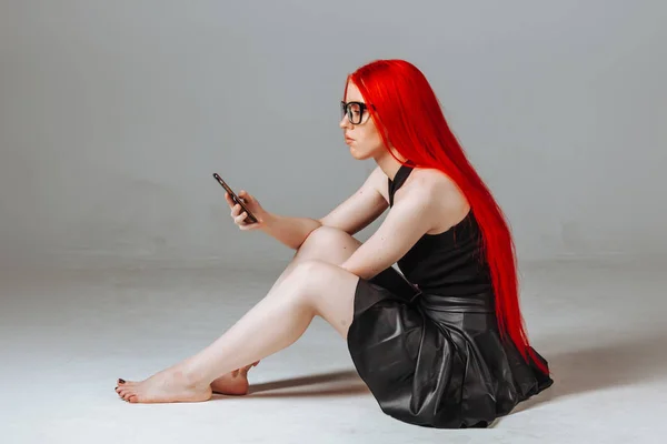 Una chica con el pelo largo rojo con gafas y una falda de cuero si —  Fotos de Stock