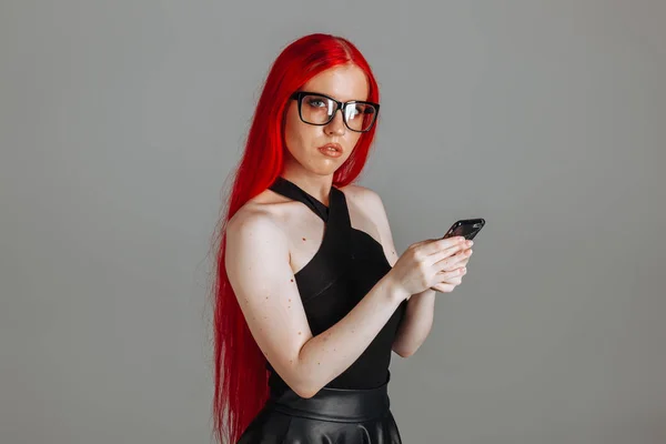 Uma menina com cabelos longos vermelhos usando óculos e uma saia de couro é — Fotografia de Stock