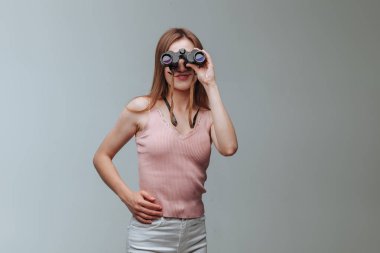 Gri bir arka plan üzerinde dürbün ile bakarak kız