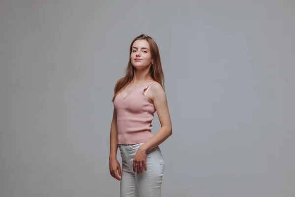 Girl in pink t-shirt and white pants on a gray background — Stock Photo, Image