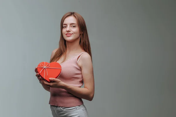 Menina segurando uma caixa de presente do coração no fundo cinza — Fotografia de Stock