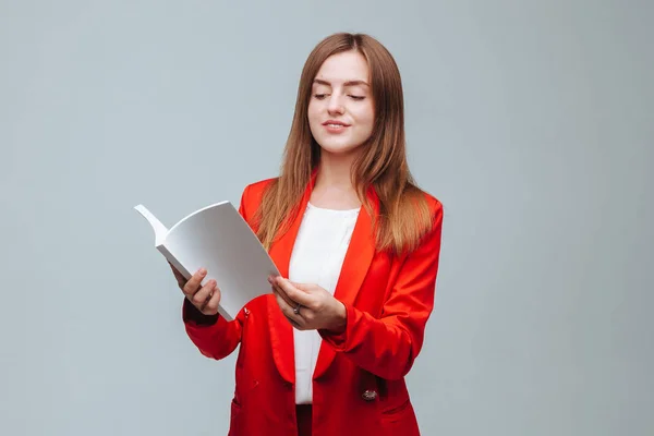 Girl in a red jacket reading a book on a gray background — Stock Photo, Image