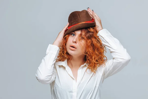 Červenovlasá radostná dívka v hnědém klobouku na šedém pozadí v — Stock fotografie