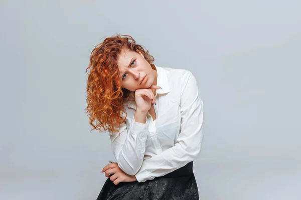 Red headed girl in white shirt thinks on light gray background — Stock Photo, Image