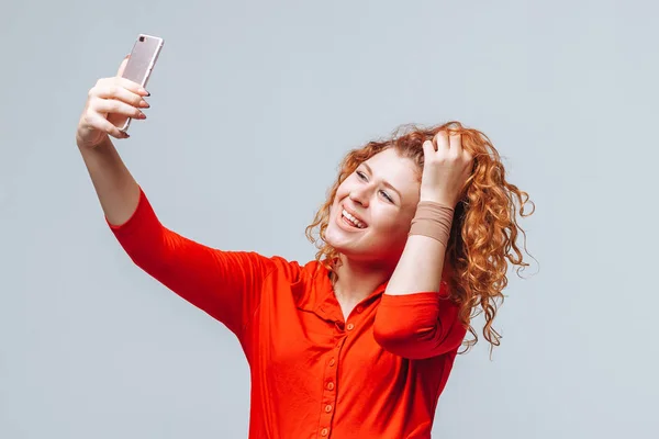 Menina ruiva leva uma selfie no telefone em um cinza claro de volta — Fotografia de Stock