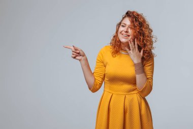 Kızıl saçlı kız açık gri arka planı işaret ediyor. Kopya sp