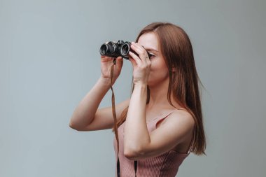 Gri bir arka plan üzerinde dürbün ile bakarak kız