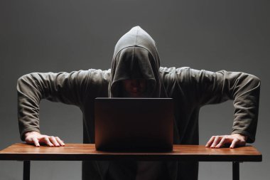 Karanlık bir arka plan üzerinde bir dizüstü bilgisayar ile bir kapüşonlu Hacker