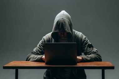 Karanlık bir arka plan üzerinde bir dizüstü bilgisayar ile bir kapüşonlu Hacker