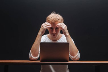 adam siyah bir arka plan üzerinde beyaz bir t-shirt bir dizüstü bilgisayar da düşünüyor