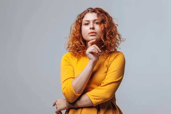 Redhaired curly girl Thinks on a light gray background