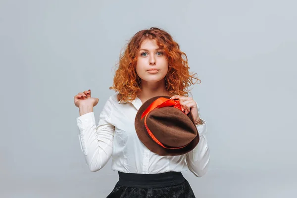 Una chica pelirroja con un sombrero marrón sonríe sobre un fondo gris —  Fotos de Stock