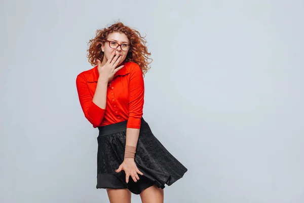 Chica pelirroja rizada en falda roja y gafas sorprendidas —  Fotos de Stock