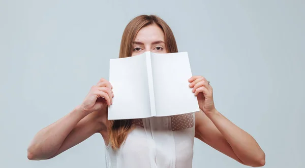 Chica cubrió su cara con un libro con una cubierta blanca en una b gris —  Fotos de Stock